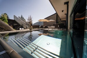 An infinity pool with a clear view of the mountains, outdoor seating, and a staircase leading to a wooden deck.