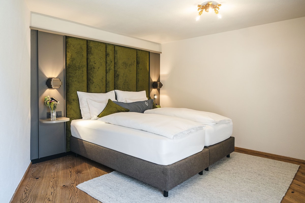 A modern bedroom with a large bed, two bedside tables, and a green accent wall.
