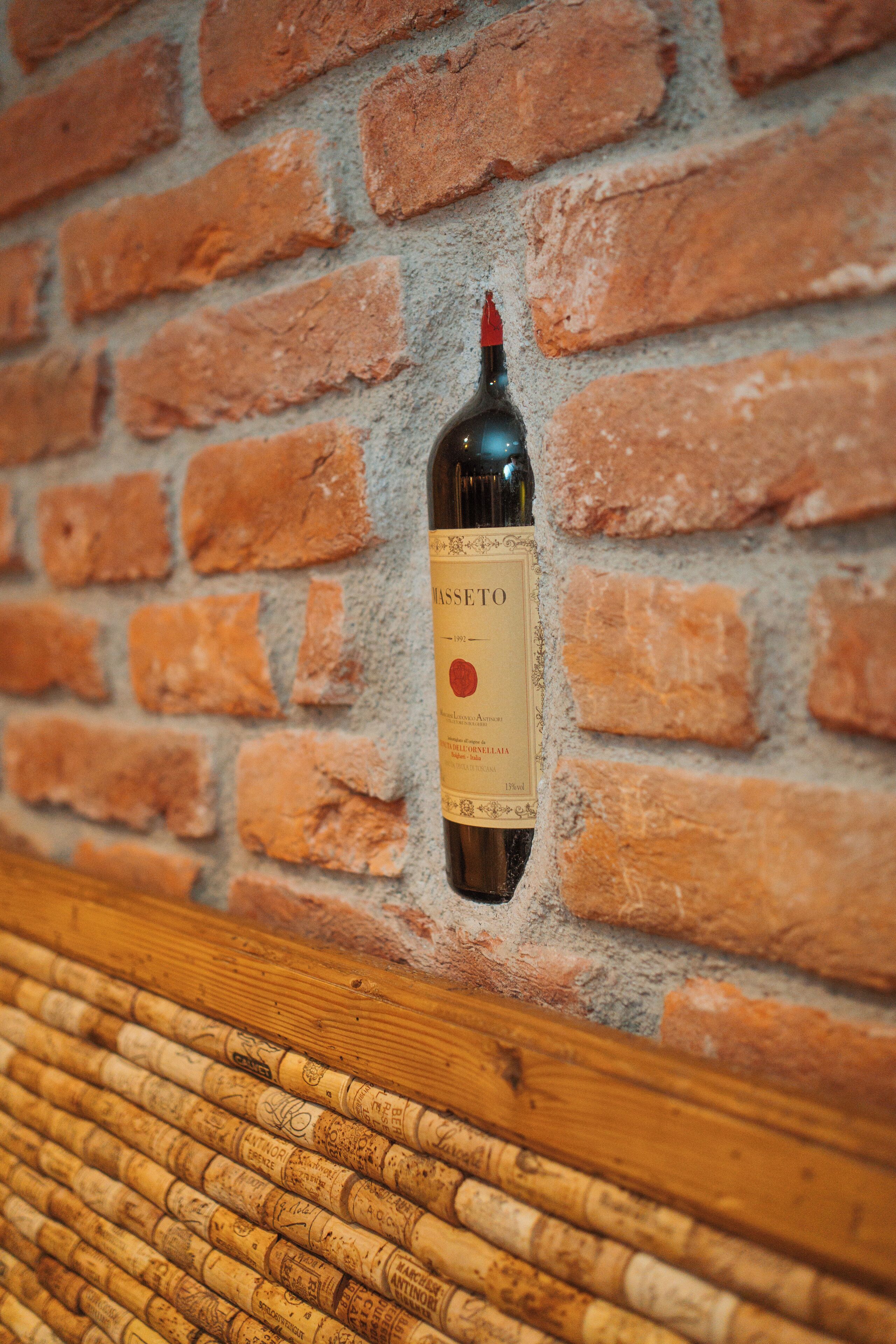 A bottle of wine against a brick wall with a wooden surface below.