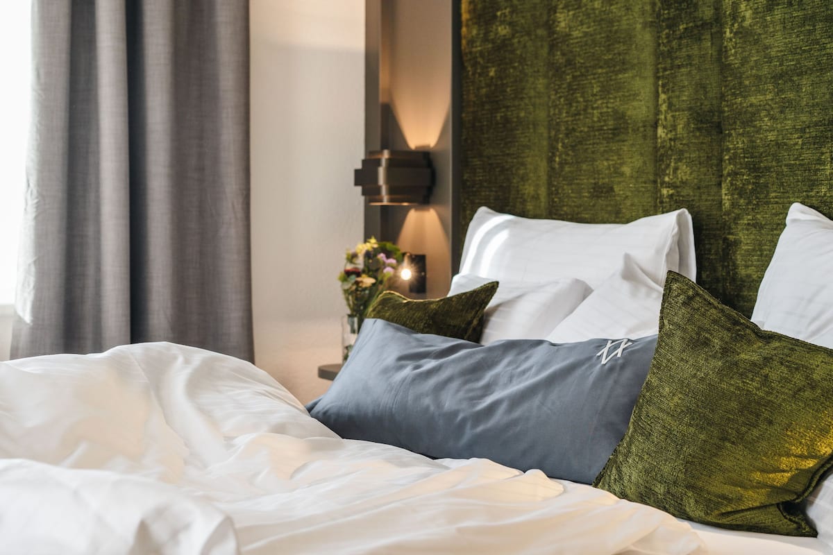 A neatly made bed with white and grey bedding, green pillows, and a green headboard.
