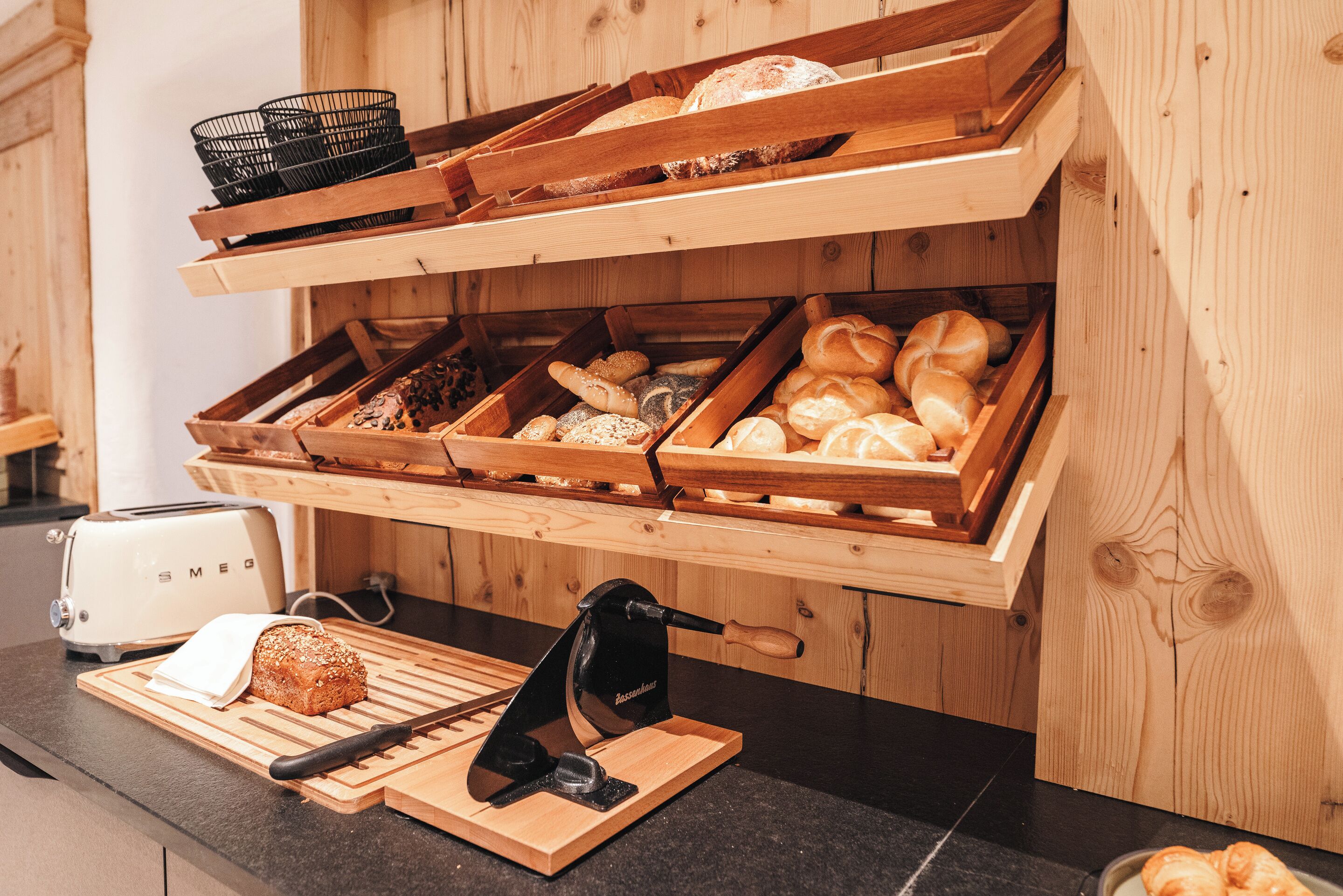A bakery display with various baked goods, a toaster, and a bread slicer on a wooden counter.