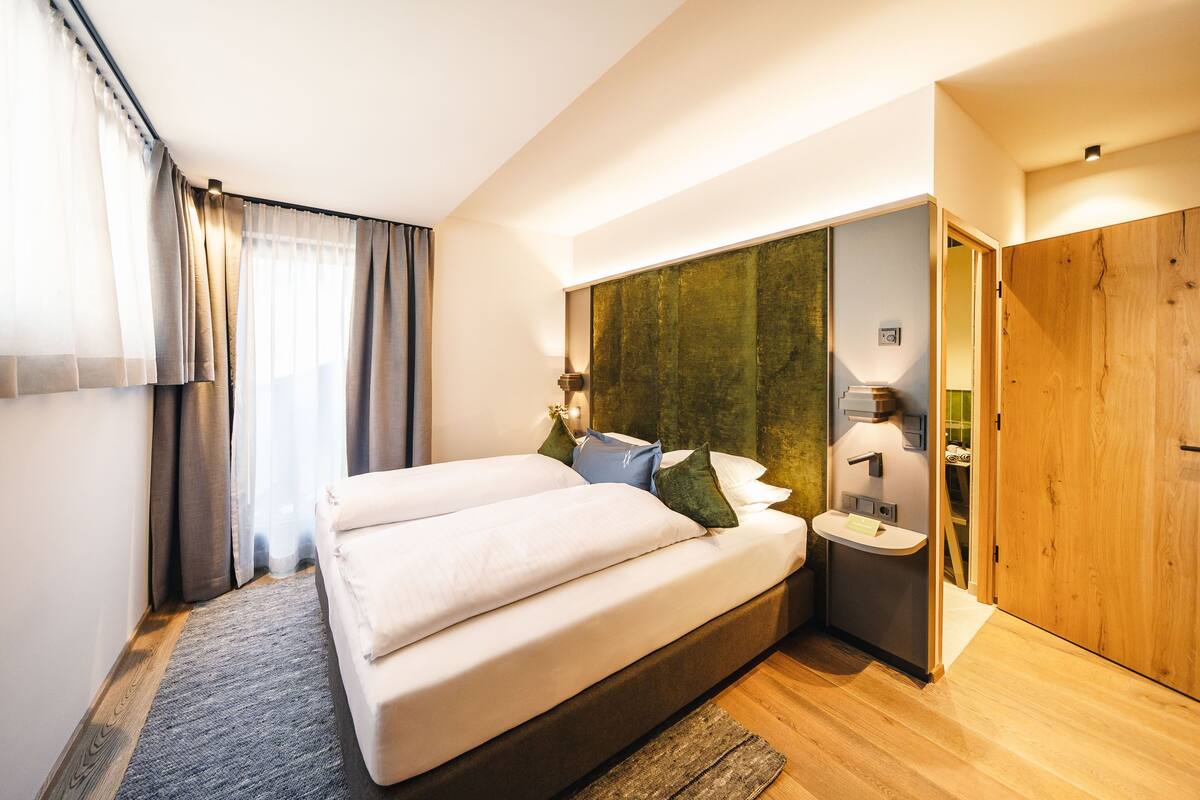 A modern bedroom with a large bed, bedside tables, a mirror, and a wooden door.