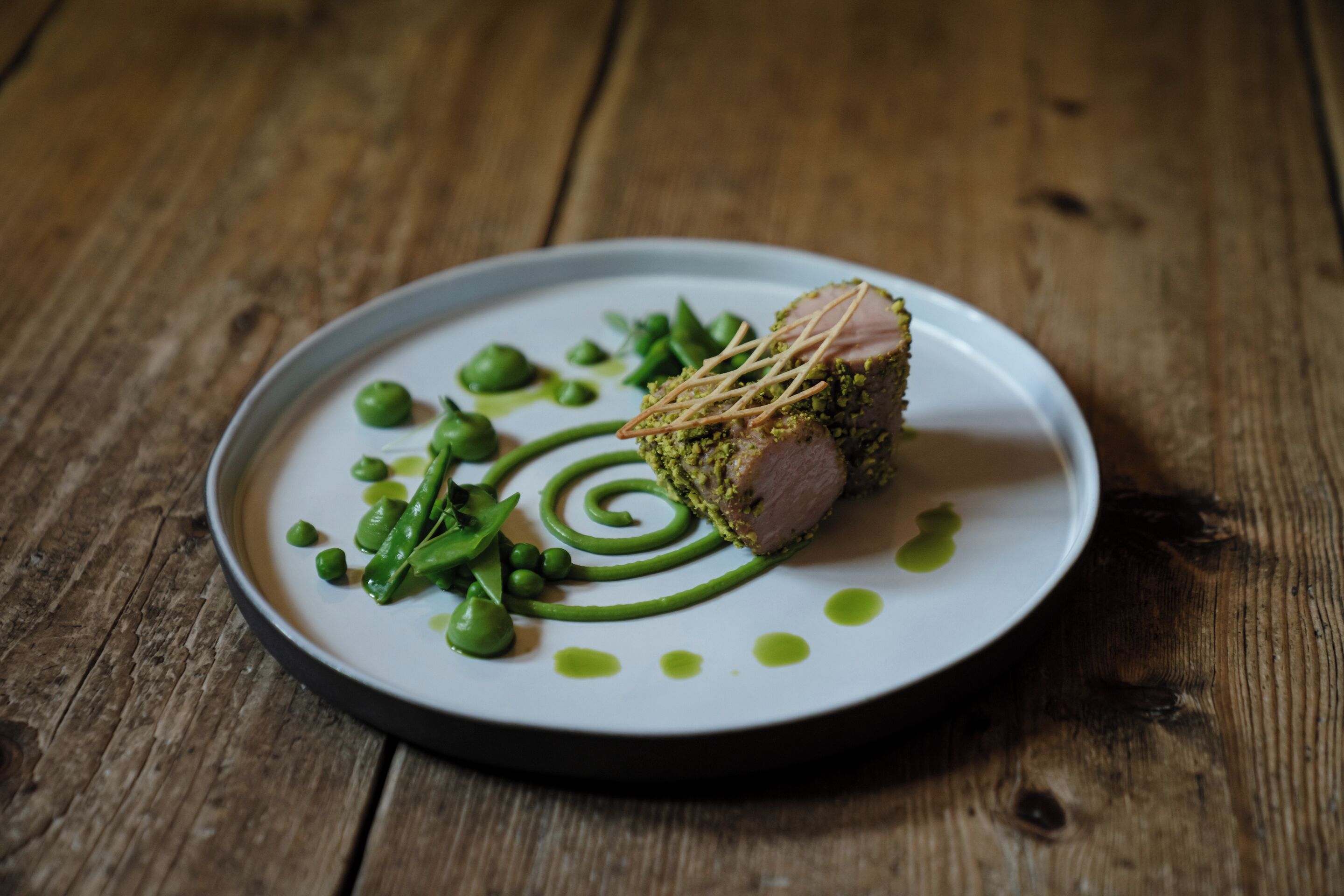 A plate with a piece of meat, green peas, and a decorative swirl on a wooden table.