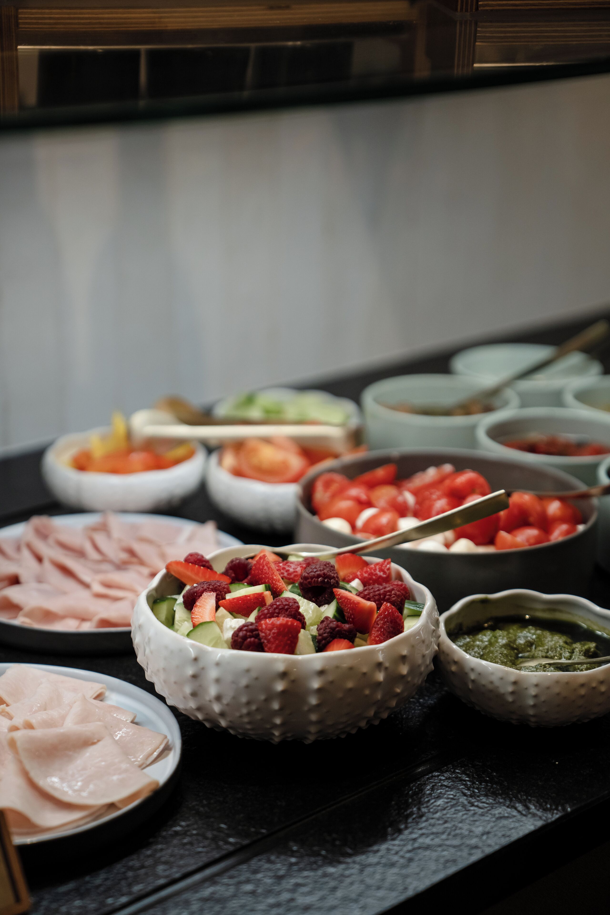 A buffet table with various food items including sliced meats, fresh fruits, and dips.