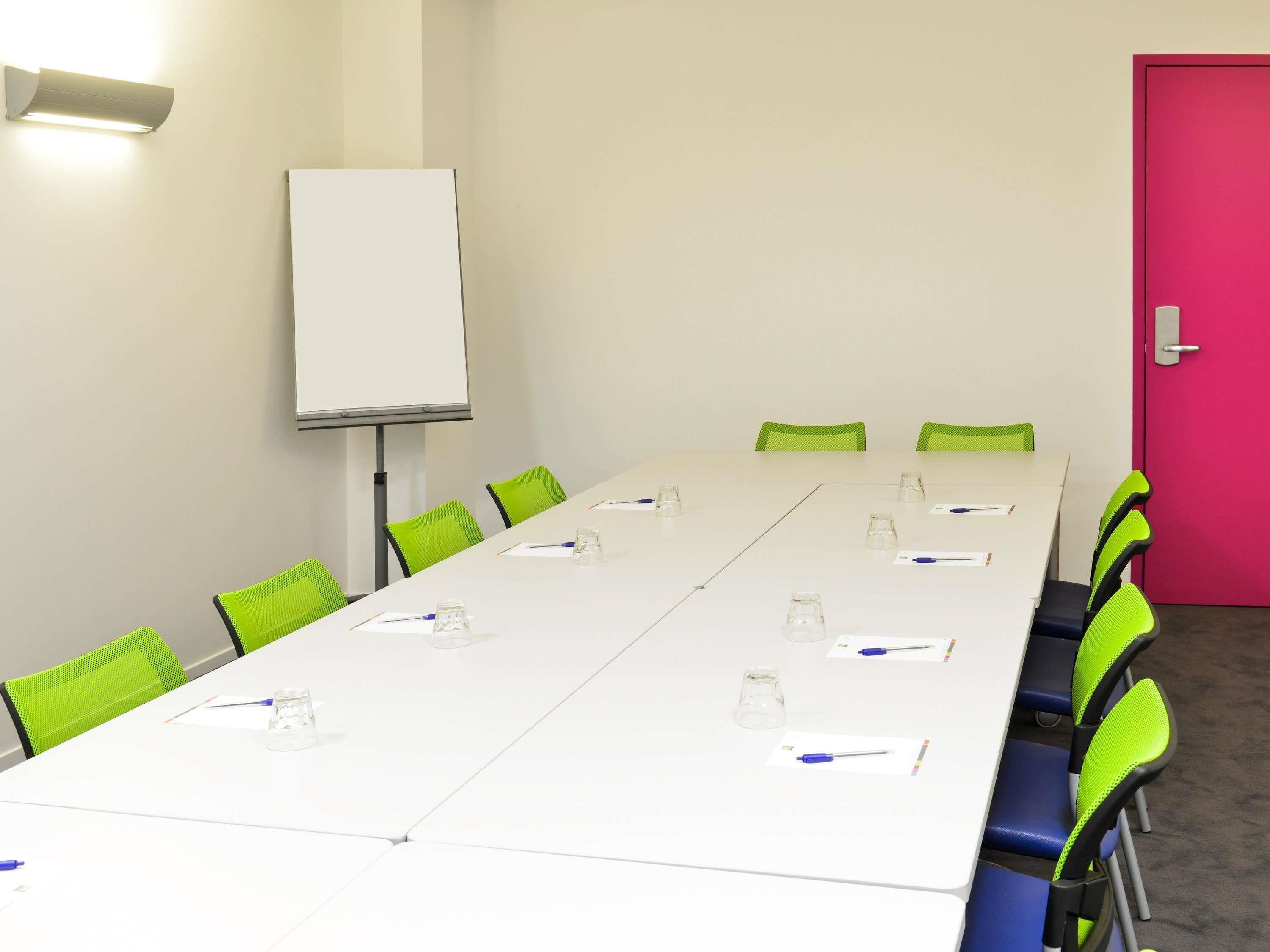 Un salón de conferencias con una larga mesa, sillas verdes, una pizarra y una puerta rosa brillante.