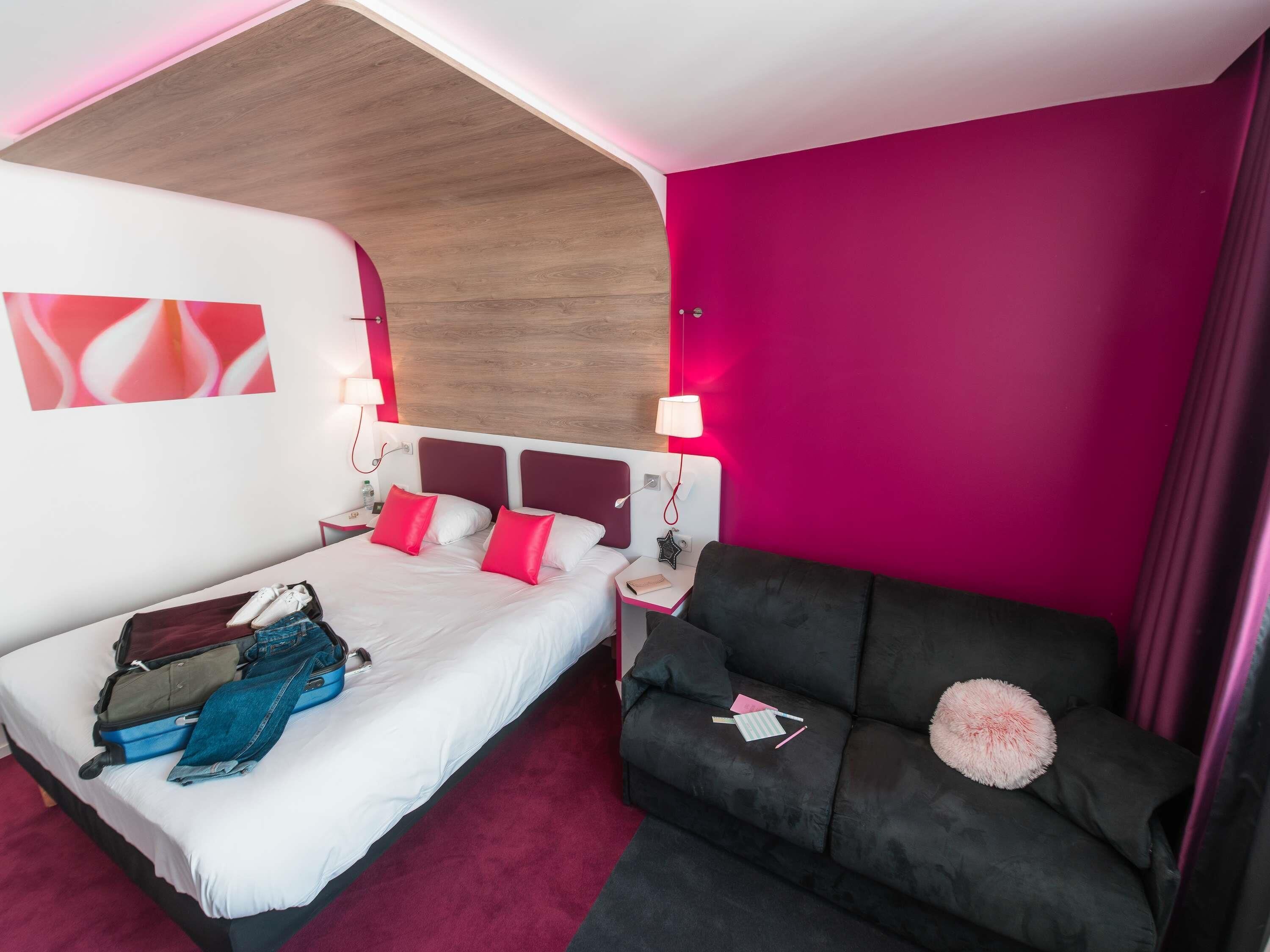 Una habitación de hotel con una cama, un sofá, techo de madera y pared rosa.