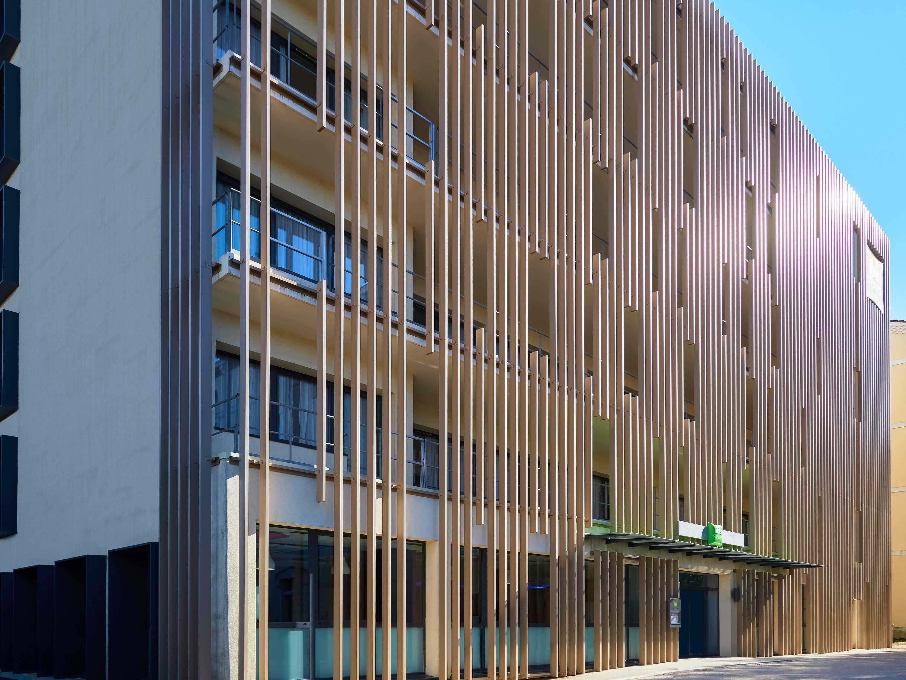 Un bâtiment moderne avec des lambris en bois verticaux, de grandes fenêtres et une enseigne verte.
