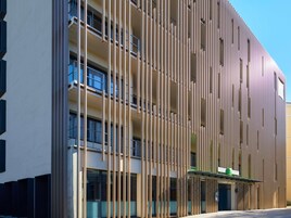 Un edificio moderno con listones verticales de madera, ventanas amplias y un letrero verde.