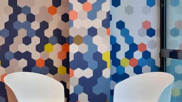Una habitación con dos sillas blancas, una pequeña mesa redonda y un pared con un patrón hexagonal de colores.