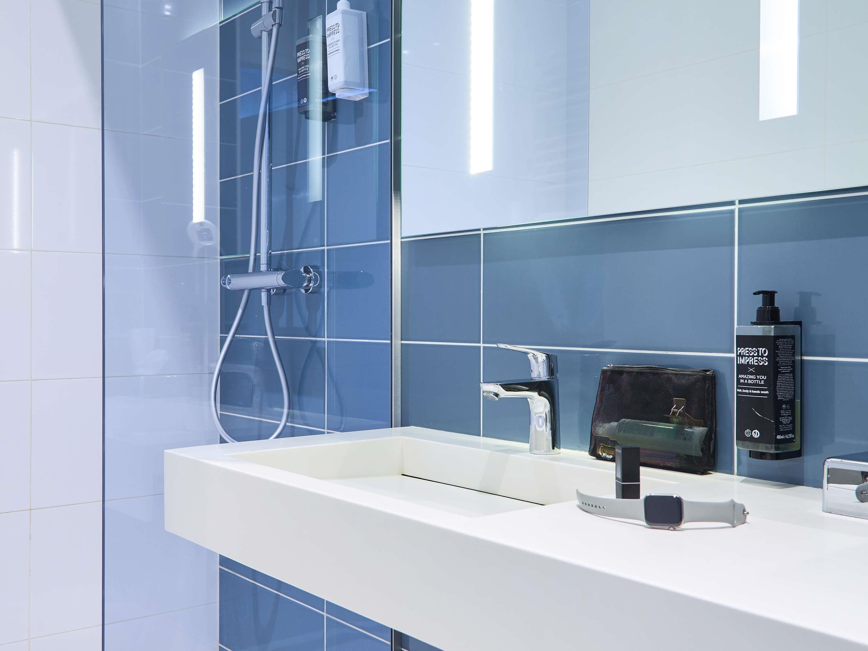 A modern bathroom with a white sink, a mirror, and a shower area.