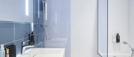 A modern bathroom with a large mirror, a white sink, a shower area, and a glass partition.