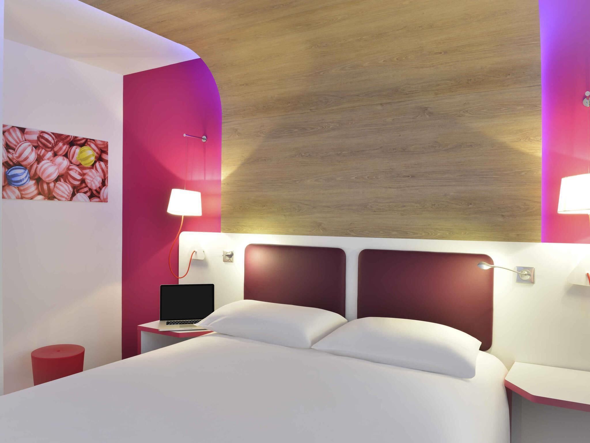A modern hotel room with a bed, a desk with a laptop, and two bedside lamps.