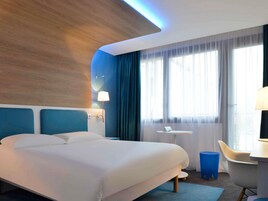 Una habitación de hotel moderna con una cama grande, una mesita pequeña, una silla y un escritorio con una lámpara.