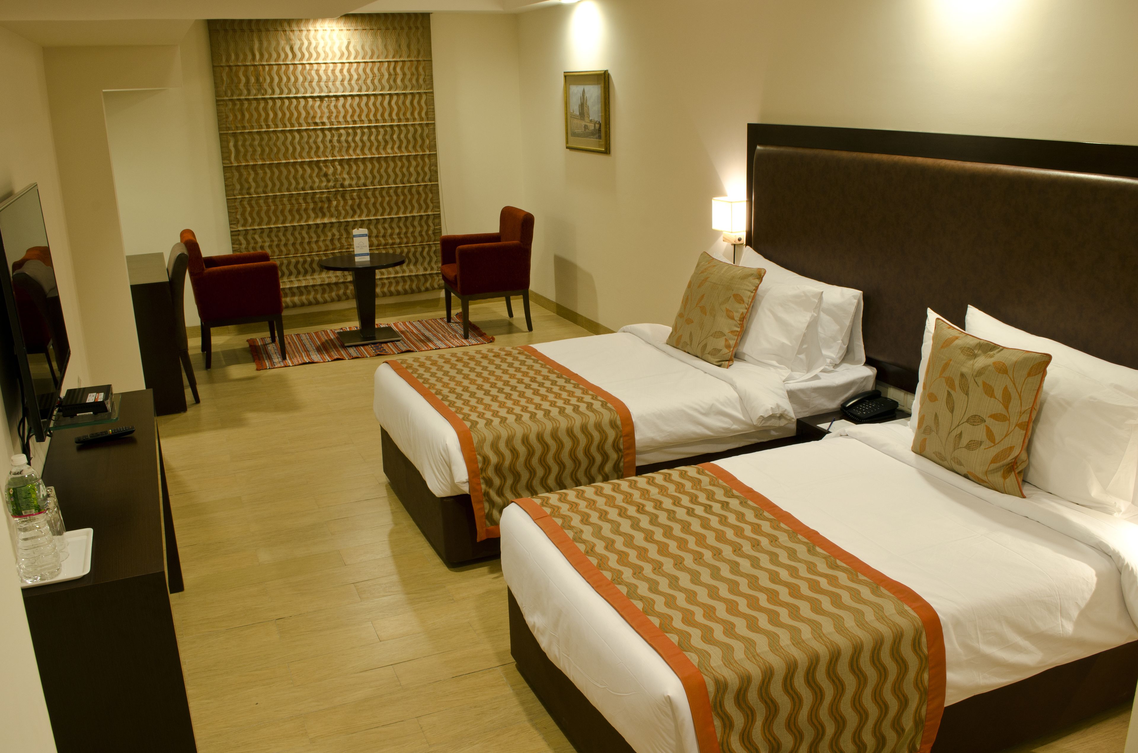 A hotel room with two beds, a desk, a chair, a small table, and a wall with a patterned design.
