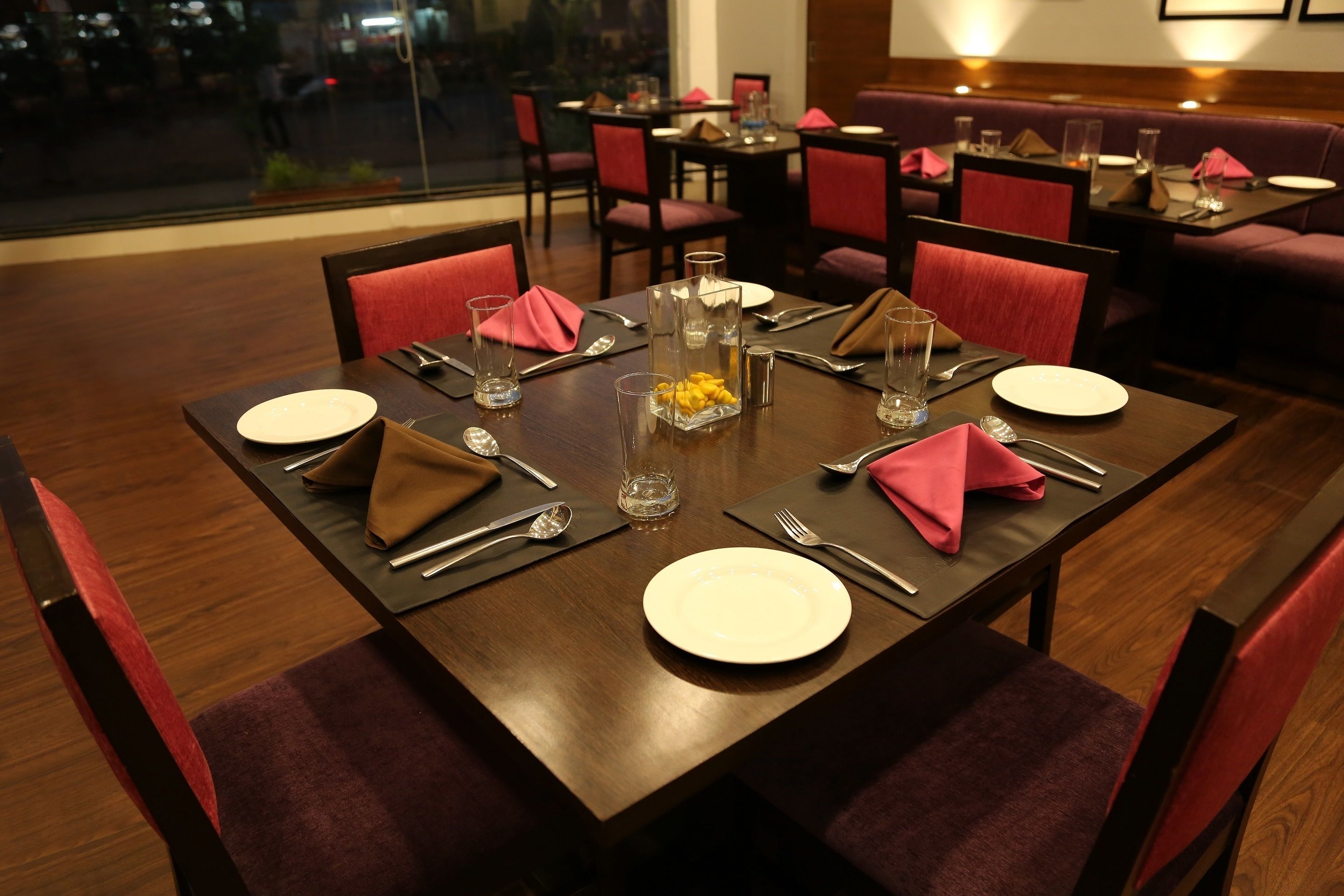 A dining area with tables set for four, each with a white plate, cutlery, and napkins.