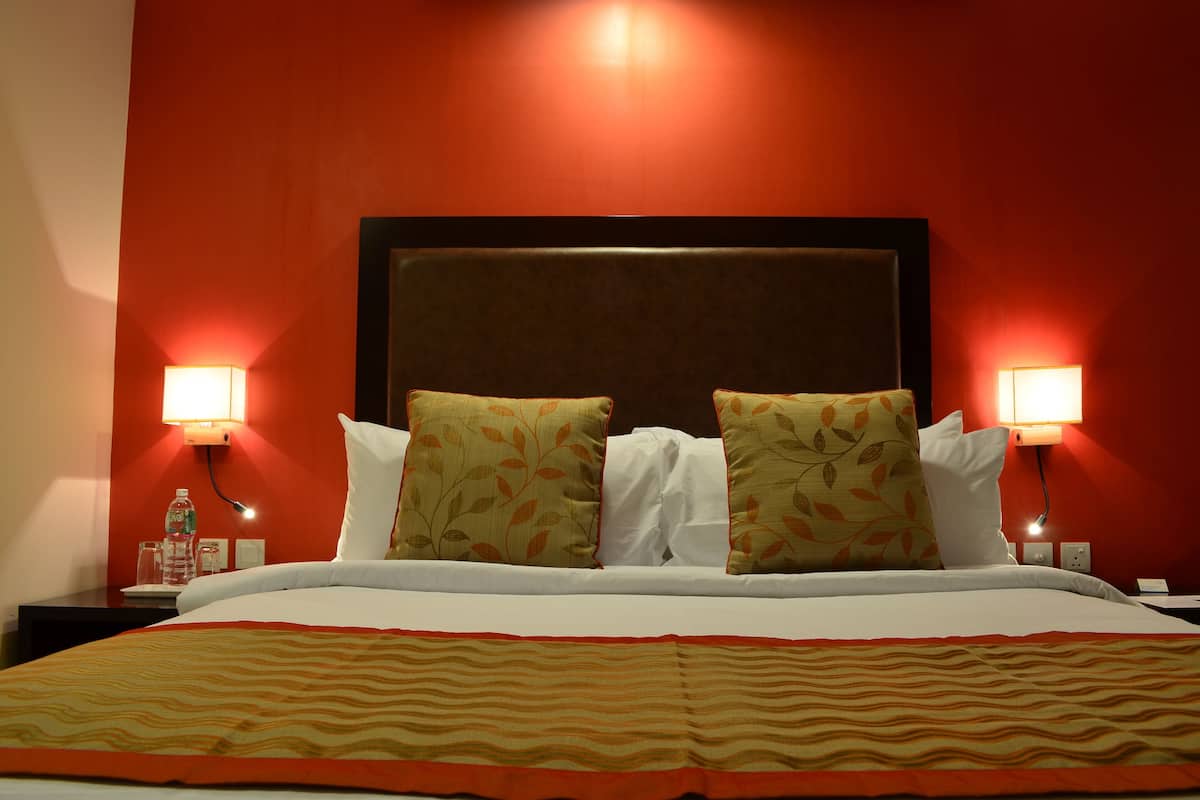 A hotel room with a large bed, two pillows, a headboard, and bedside lamps.