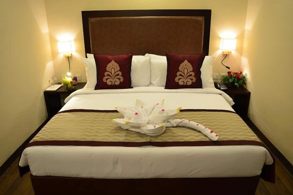 A hotel room with a large bed, two bedside lamps, a nightstand with a phone and a vase of flowers, and a decorative towel on the bed.