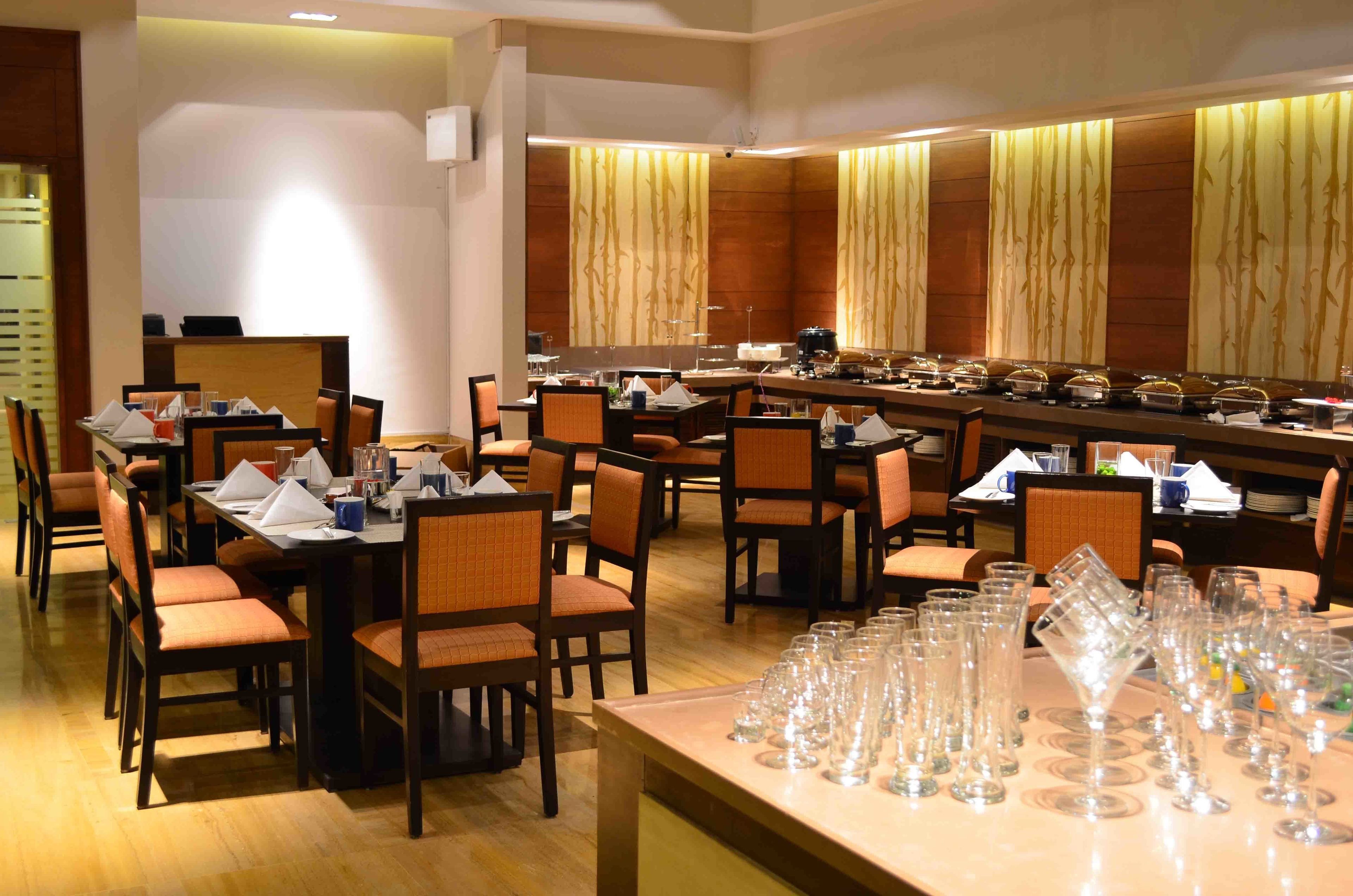 A restaurant with multiple tables and chairs, a buffet area with food items, and a bar.