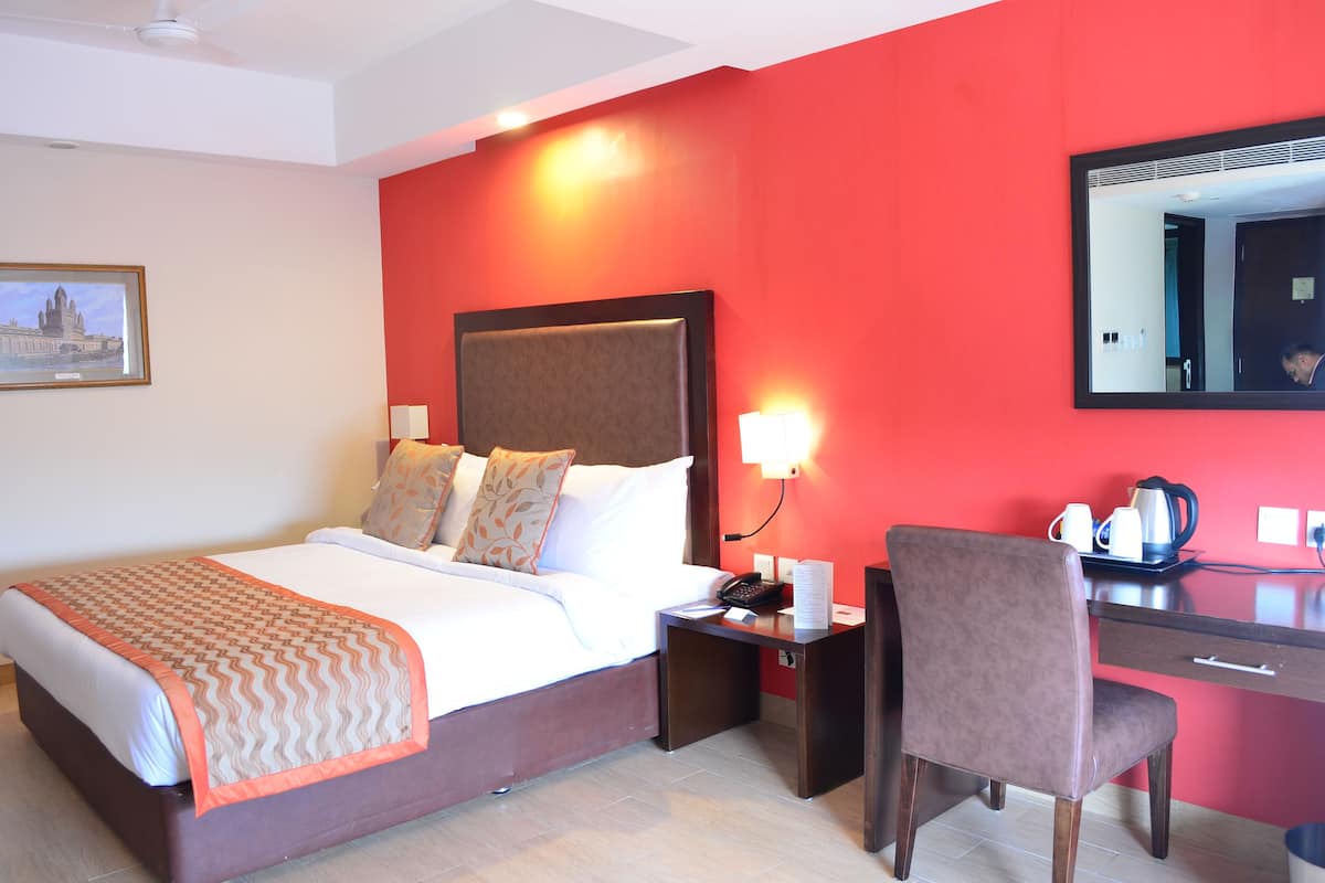 A hotel room with a bed, bedside table, chair, and a desk with a mirror.