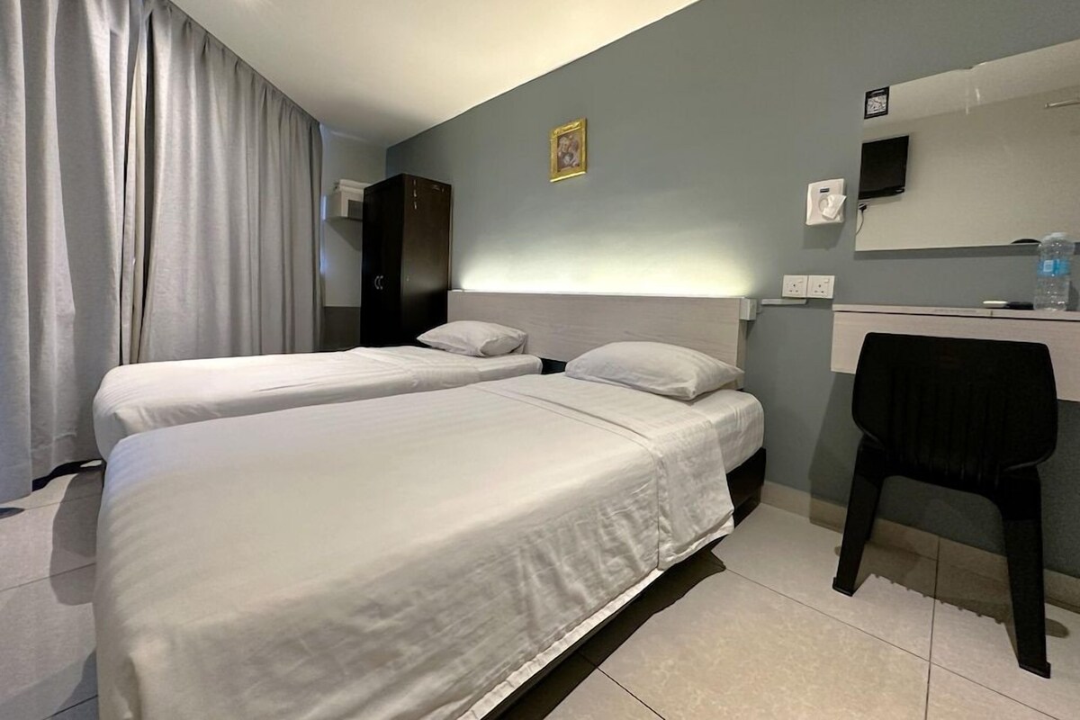 Une chambre d’hôtel avec deux lits, un bureau avec une chaise, une télévision et une fenêtre avec des rideaux.