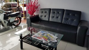 Ein modernes Wohnzimmer mit einer schwarzen Ledersofa, einem Glastisch mit Zeitungen und einer blühenden roten Pflanze.