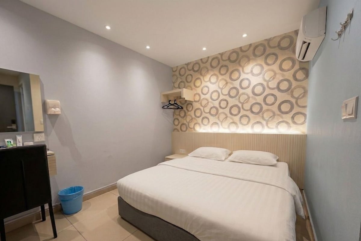Une chambre à coucher avec un lit, un bureau, une poubelle bleue et un mur à motifs.