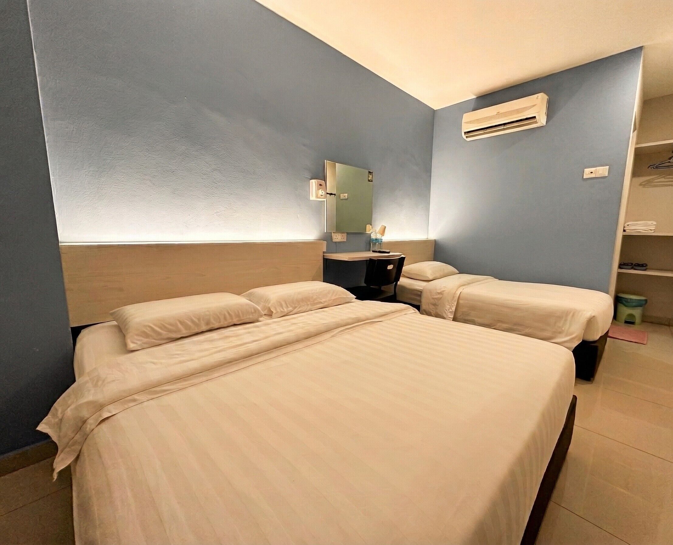 A hotel room with two beds, a desk, a chair, a mirror, an air conditioning unit, and a shelf with items.