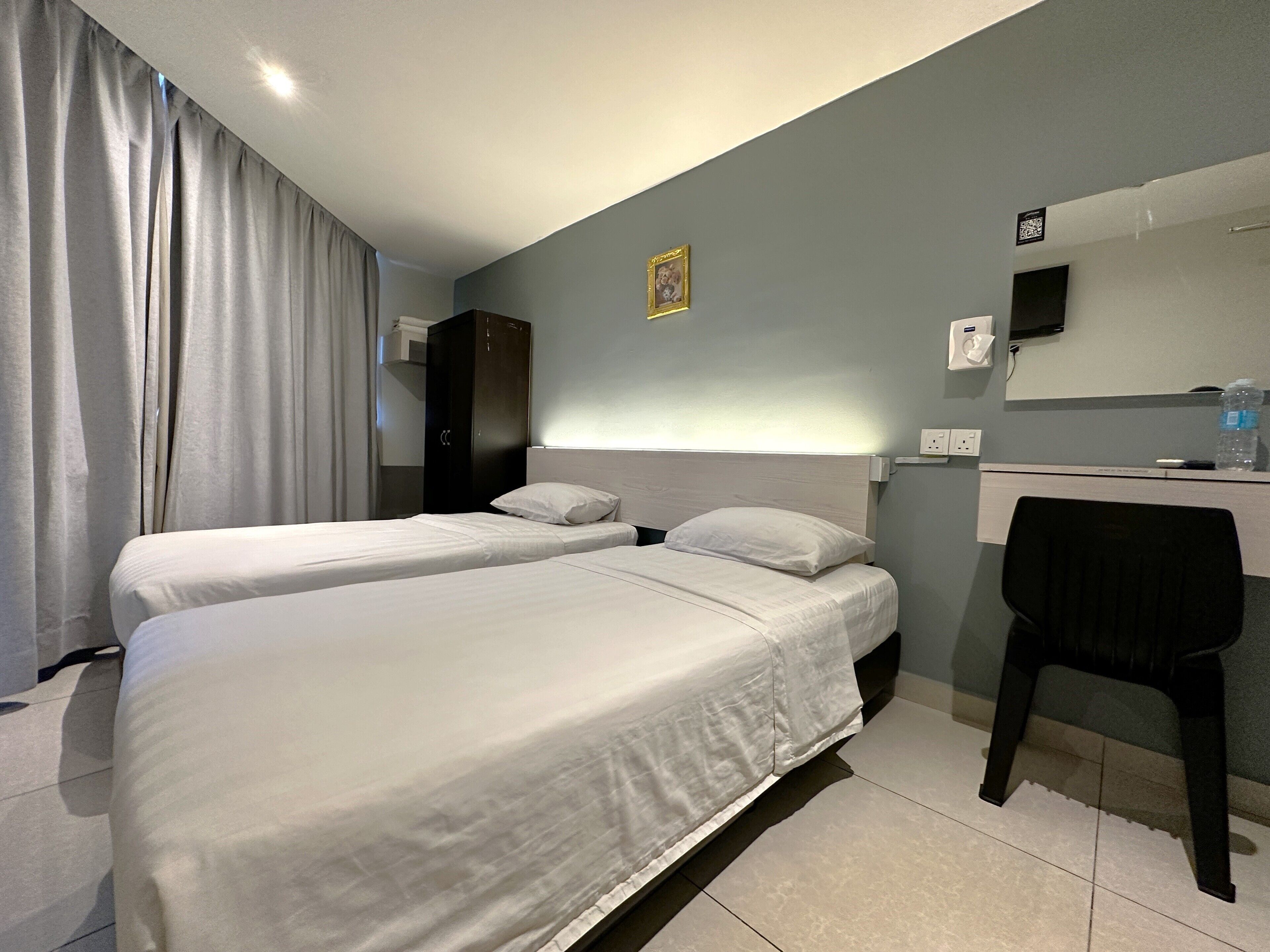 A hotel room with two beds, a desk, a chair, a wardrobe, and a mirror.
