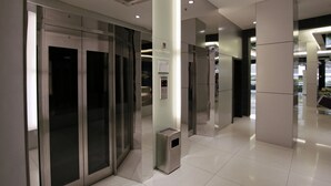 Un ascensor moderno con puertas metálicas y un pequeño cubo de basura a su lado.