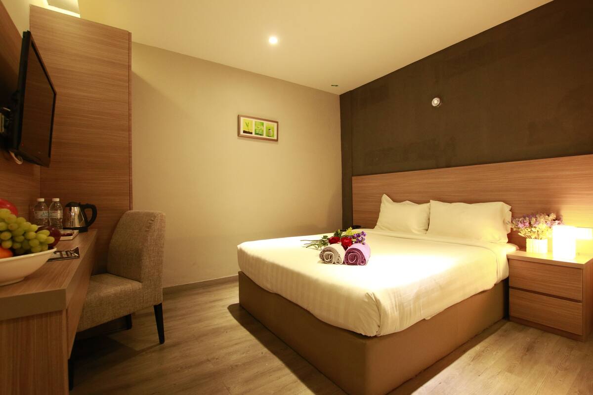 Een hotelkamer met een bed, nachtkastje, stoel en een klein bureau met een fruitschaal en een koffiezetapparaat.