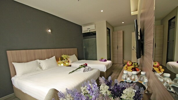 Una habitación de hotel con una cama grande, una mesita de noche con fruta y botellas, y un espejo.