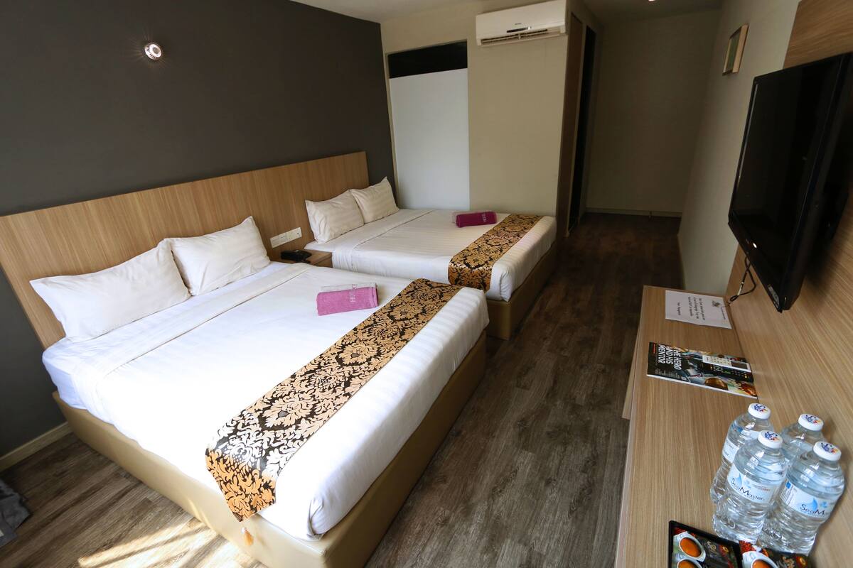 Een hotelkamer met twee bedden, een televisie, een bureau met waterflesjes en een poster.