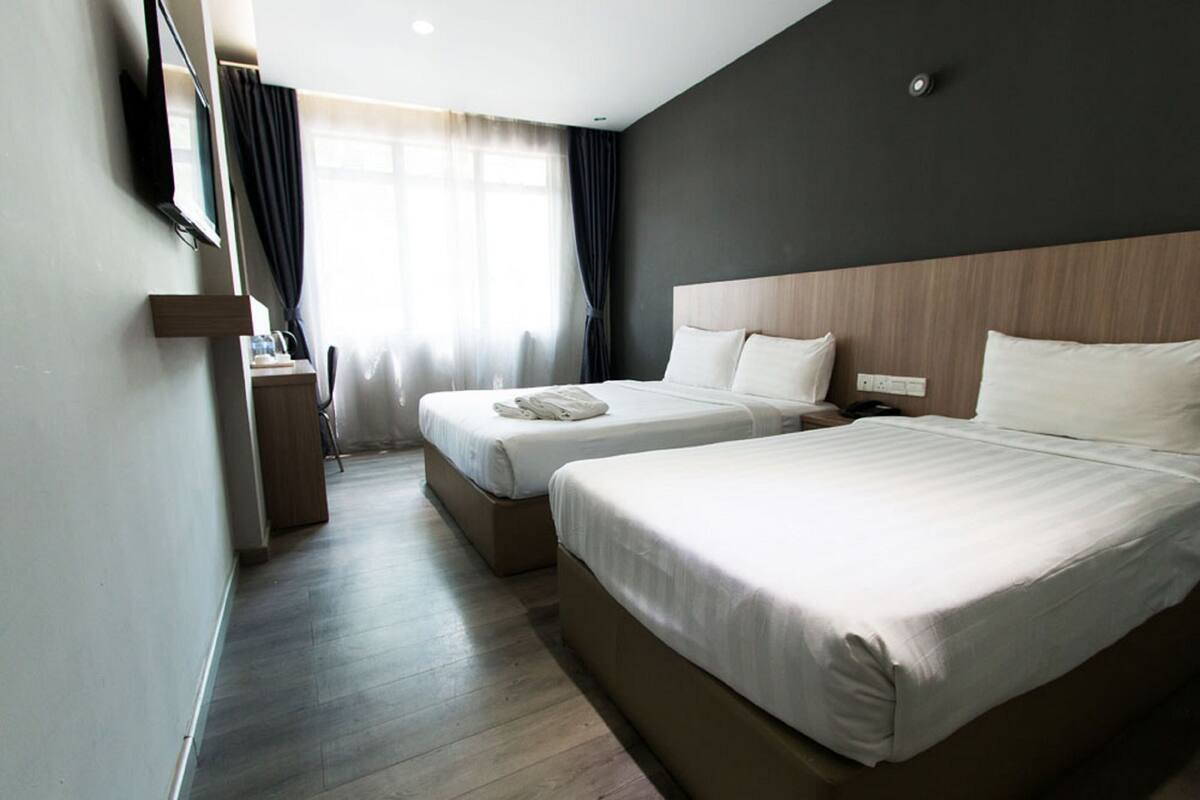 Een hotelkamer met twee bedden, een flatscreen televisie aan de muur en een raam met gordijnen.