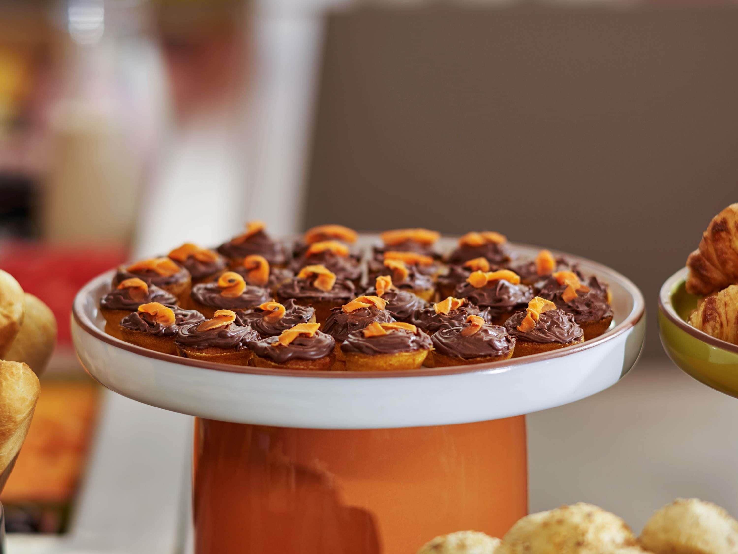 Un plateau de desserts avec des pâtisseries nappées de chocolat et des morceaux d’orange caramélisés, le tout présenté sur un présentoir en céramique.
