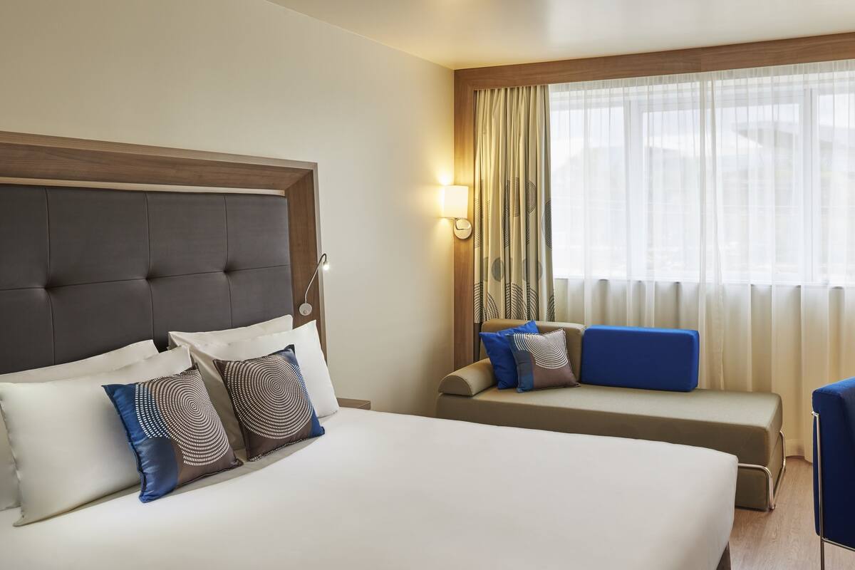 Une chambre d’hôtel avec un grand lit, un petit canapé, un bureau et une fenêtre avec des rideaux.