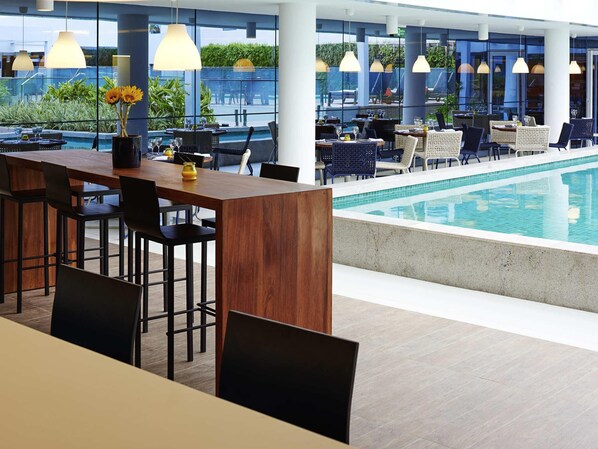 Un bar situé au bord de la piscine, avec des sièges, une piscine et de grandes fenêtres.