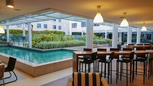 A poolside area with a dining setup, including tables and chairs, and a view of a building in the background. - Novotel Rio de Janeiro Parque Olímpico (Rio de Janeiro)
