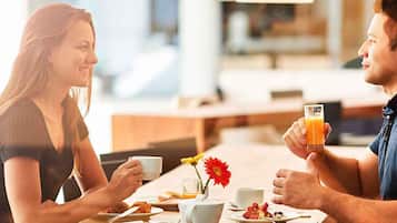 Una pareja cenando en una mesa con alimentos para el desayuno, un florero y una lámpara.