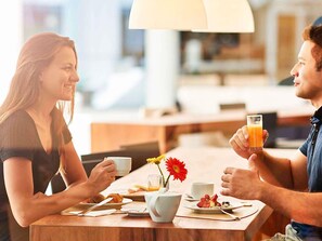A couple dining at a table with breakfast items, a flower vase, and a lamp. - Novotel Rio de Janeiro Parque Olímpico (Rio de Janeiro)