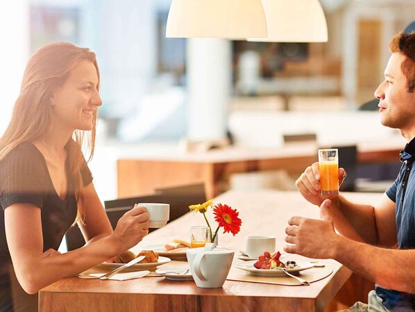 Ein Paar frühstückt an einem Tisch mit Speisen, einer Blumenvase und einer Lampe.