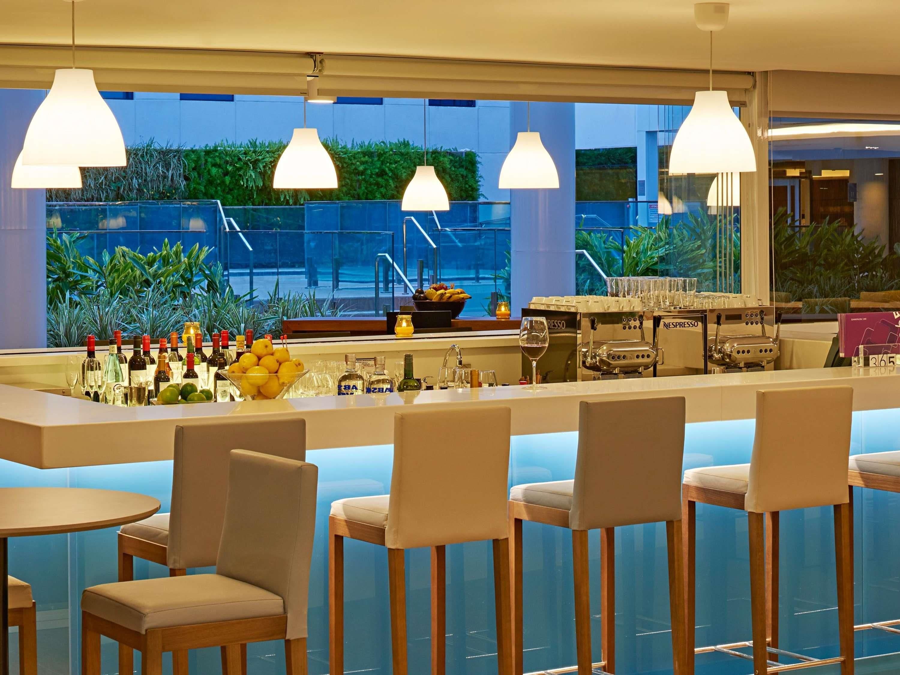 Eine Bar mit verschiedenen Sitzgelegenheiten, einer Theke voller Flaschen und Gläsern sowie Blick auf Grünflächen im Freien.