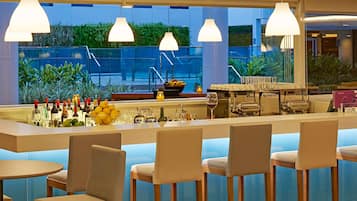 Eine Bar mit verschiedenen Sitzgelegenheiten, einer Theke voller Flaschen und Gläsern sowie Blick auf Grünflächen im Freien.
