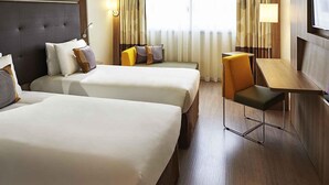 A hotel room with two beds, a desk, and a chair. There are curtains and a window providing natural light. - Novotel Rio de Janeiro Parque Olímpico (Rio de Janeiro)