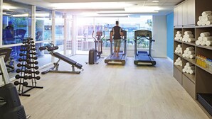 A gym with treadmills, weight machines, and a bench. There are towels and bottles on shelves. - Novotel Rio de Janeiro Parque Olímpico (Rio de Janeiro)