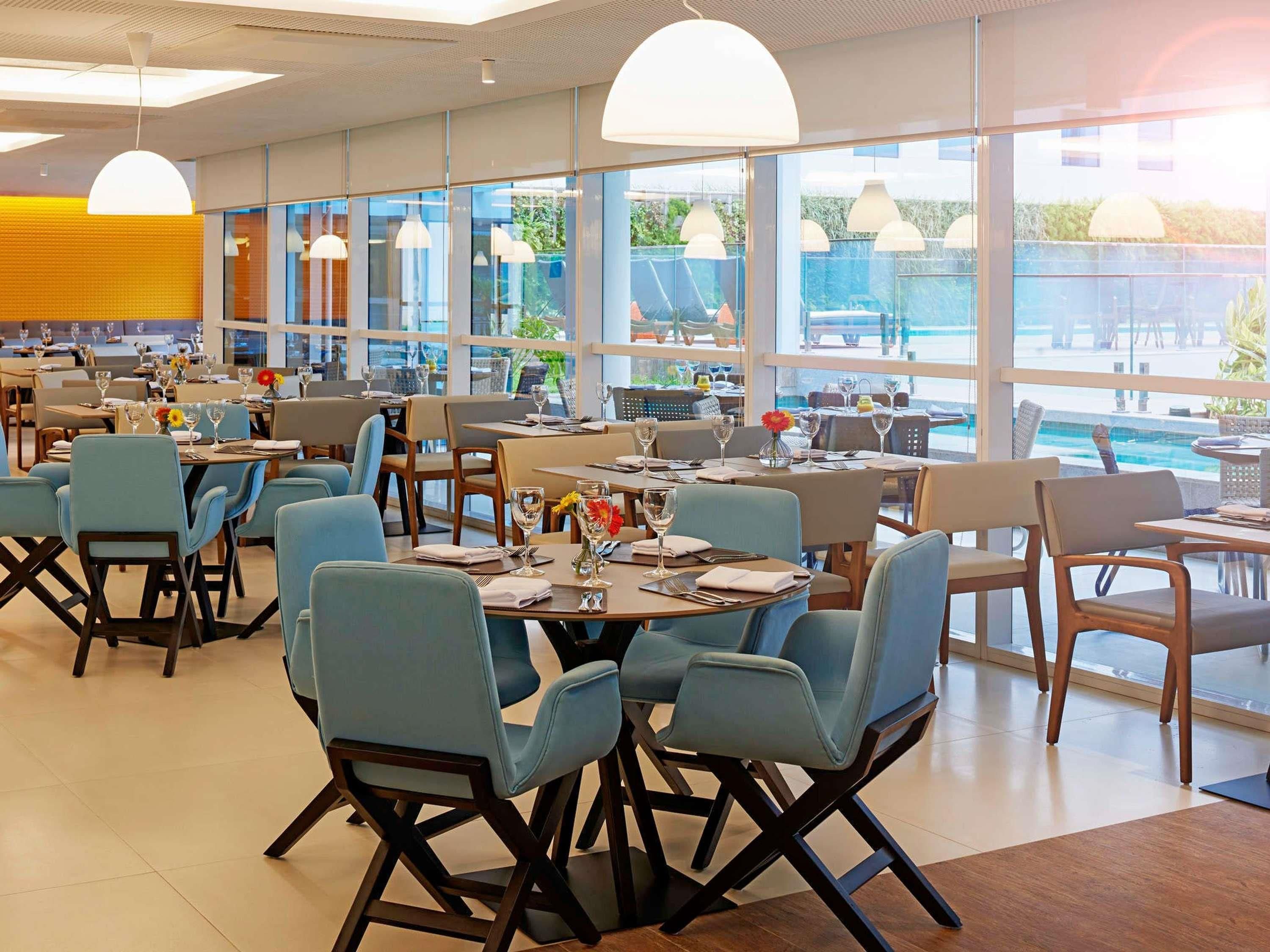 Un restaurante espacioso con varias mesas y sillas, grandes ventanales que ofrecen vistas al exterior e iluminación colgante.