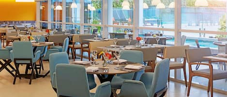 Un restaurante espacioso con varias mesas y sillas, grandes ventanales que ofrecen vistas al exterior e iluminación colgante.