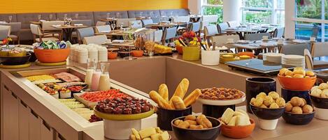 A buffet setup with various food items and beverages, a seating area with tables and chairs, and a bright interior with natural light.