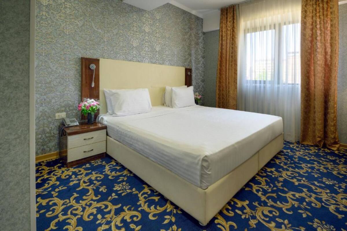 A hotel room with a large bed, a nightstand with a phone, and a window with curtains.
