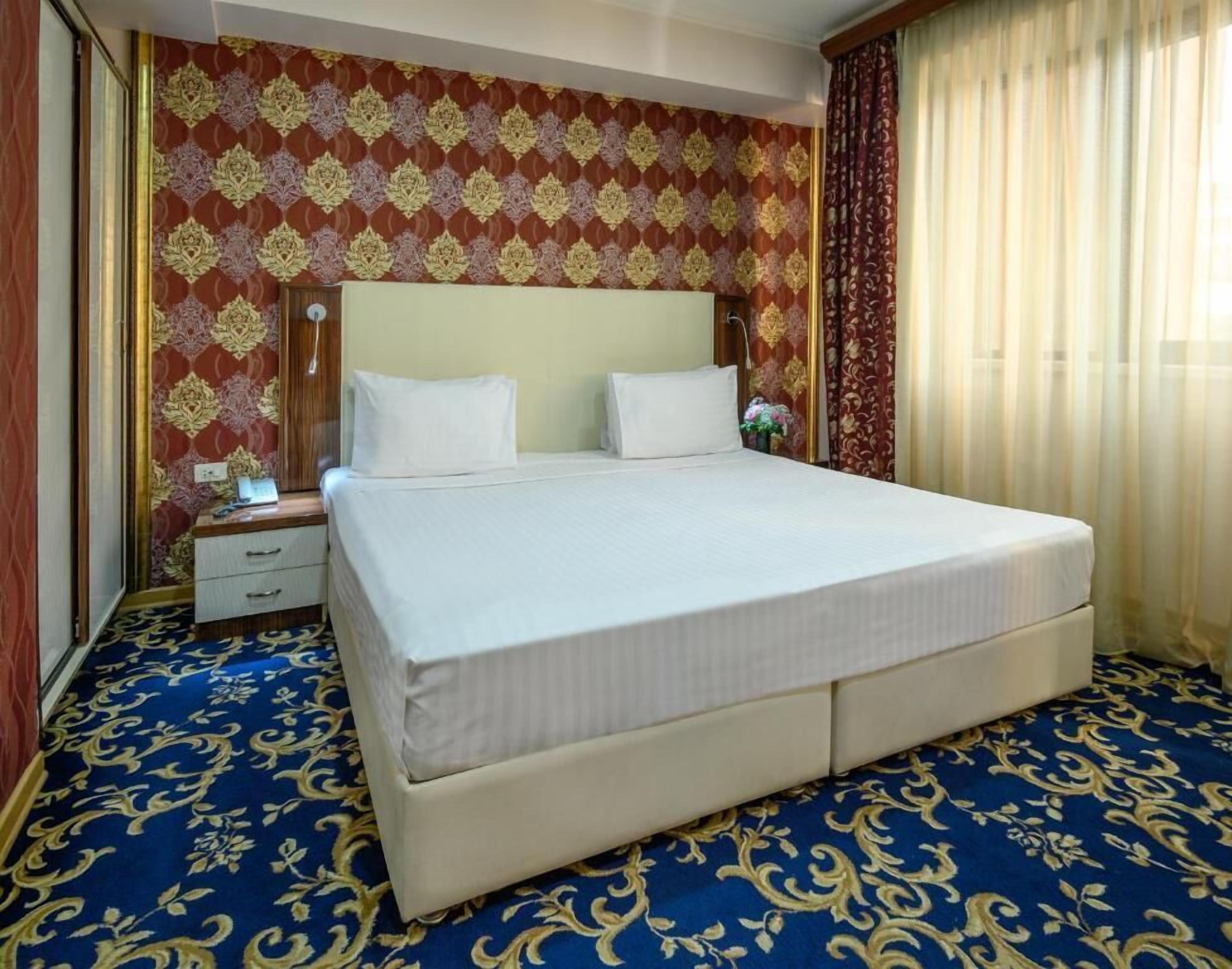 A hotel room with a large bed, a nightstand, a dresser, and a patterned carpet.