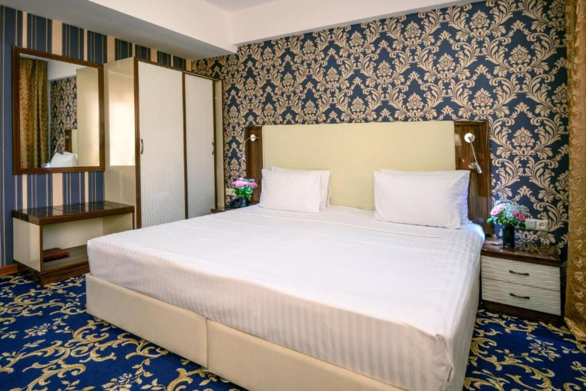 A hotel room with a large bed, a bedside table, a dresser, and a mirror.